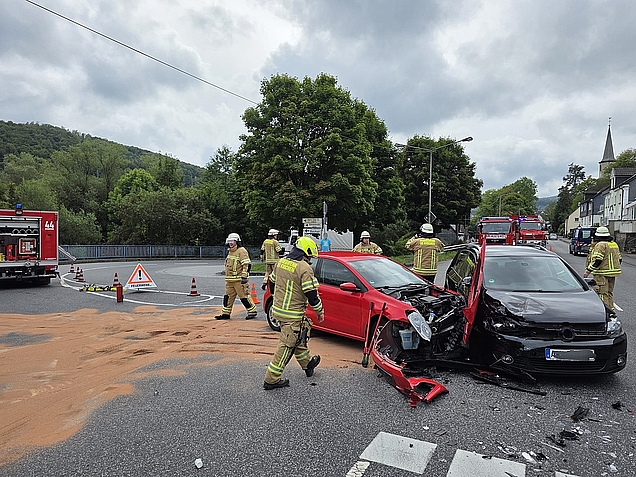 zwei verunfallte Fahrzeuge auf einer Bundesstraße mit vielen Feuerwehrleuten und Fahrzeugen drumherum, eine große Öllache ist mit Bindemittel abgestreut