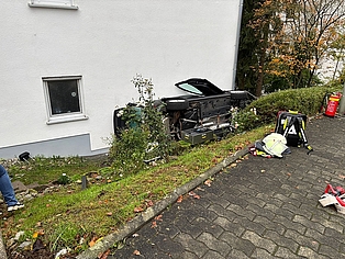 Ein Auto, dass auf der Seite an eine Hauswand gelehnt liegt. 