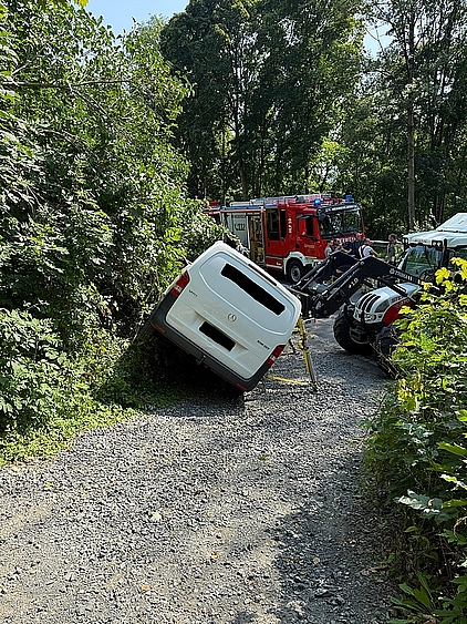 Ein Transporter, der zu kippen droht, wird von einem Traktor gestützt. Im Hintergrund steht ein Feuerwehrauto und mehrere Feuerwehrmänner.