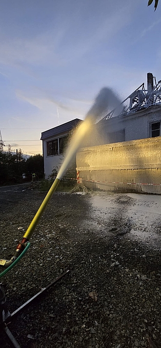 ein Schaumrohr vor einer Brandruine, aus welchem Schaum in das Gebäude abgegeben wird
