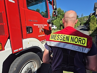 Ein Feuerwehrfahrzeug, neben dem ein Feuerwehrmann mit der Aufschrift Messen Nord auf dem Rücken steht. 