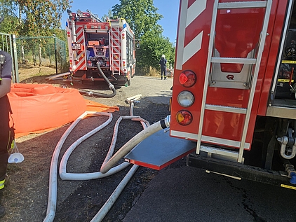 Feuerwehrauto, von dem Schläuche zu einem Sammelbecken abgehen