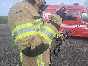 Feuerwehrmann, der funkt mit Einsatzleitwagen im Hintergrund