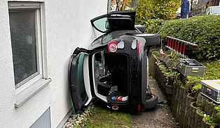 Ein Auto, dass auf der Seite an eine Hauswand gelehnt liegt. 
