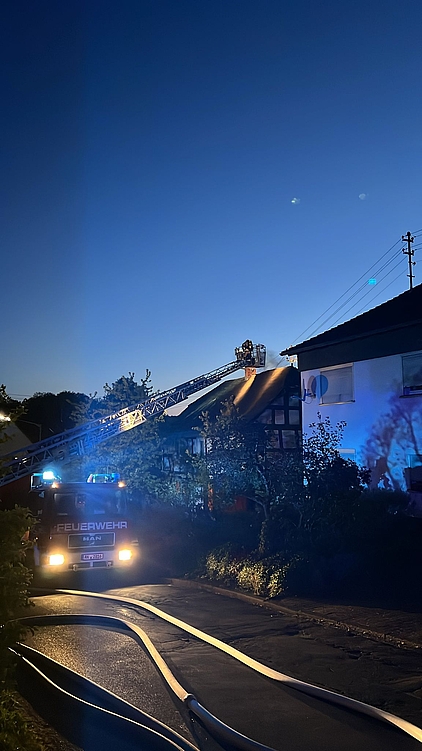 Drehleiter mit Blaulicht in der Dämmerung mit ausgefahrenem Leiterpark vor einem Haus
