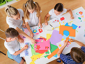 Kinder sitzen gemeinsam an einem Tisch und basteln