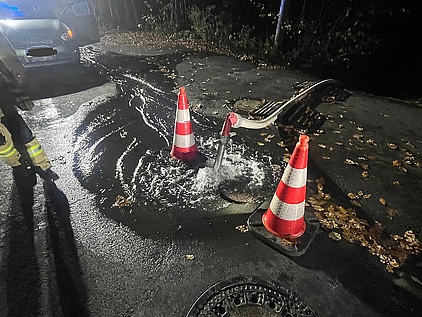 Ein Unterflurhydrant, aus dem Wasser sprudelt, abgesperrt durch Pylonen